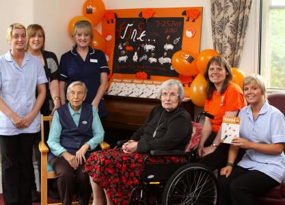 Residents and staff at Buxton's Pavilion Care Home meet chair of the Buxton Festival Fringe, Stephanie Billen (in orange), to unveil a special wall display made by the residents to celebrate the Fringe. Pictured clockwise from top left: care assistant Julie Standidge, activity co-ordinator Amy Moss, home manager Jayne Davidson-Pinder, Stephanie Billen, care assistant Leah Kenny, resident Sandra Shilton (in wheelchair) and resident Ivy Tongue. (Credit: Jason Chadwick. By kind permission of Buxton Advertiser)