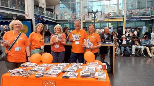 Pam, Stephanie, Helen, Rob and Catherine promote train and bus travel to Buxton Fringe at Piccadilly Station in Manchester. With thanks to High Peak and Hope Valley Community Rail Partnership (credit: Ian Bowns 2026) 